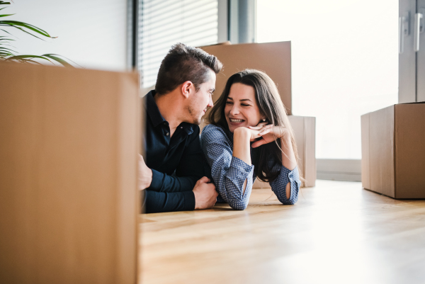 A young happy couple with a cup and cardboard boxes lying on a floor, moving in a new home.