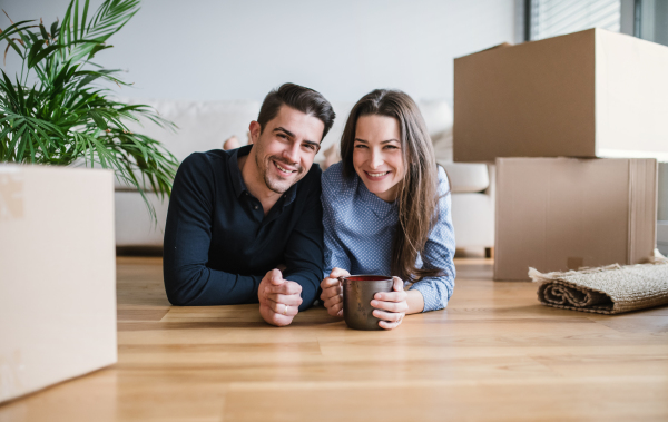 A young happy couple with a cup and cardboard boxes lying on a floor, moving in a new home.