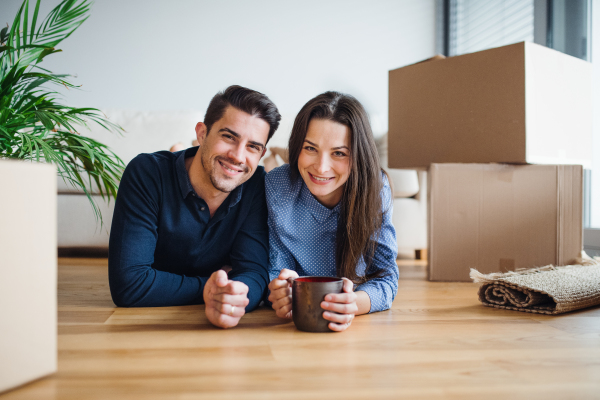 A young happy couple with a cup and cardboard boxes lying on a floor, moving in a new home.