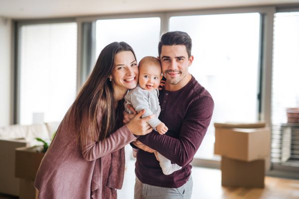 A portrait of happy young couple with a baby and cardboard boxes, moving in a new home.