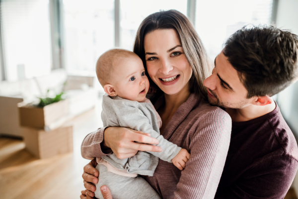 A portrait of happy young couple with a baby and cardboard boxes, moving in a new home.