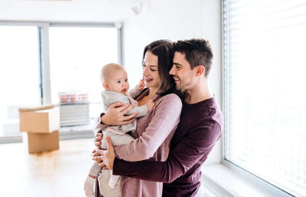 A portrait of happy young couple with a baby and cardboard boxes, moving in a new home.