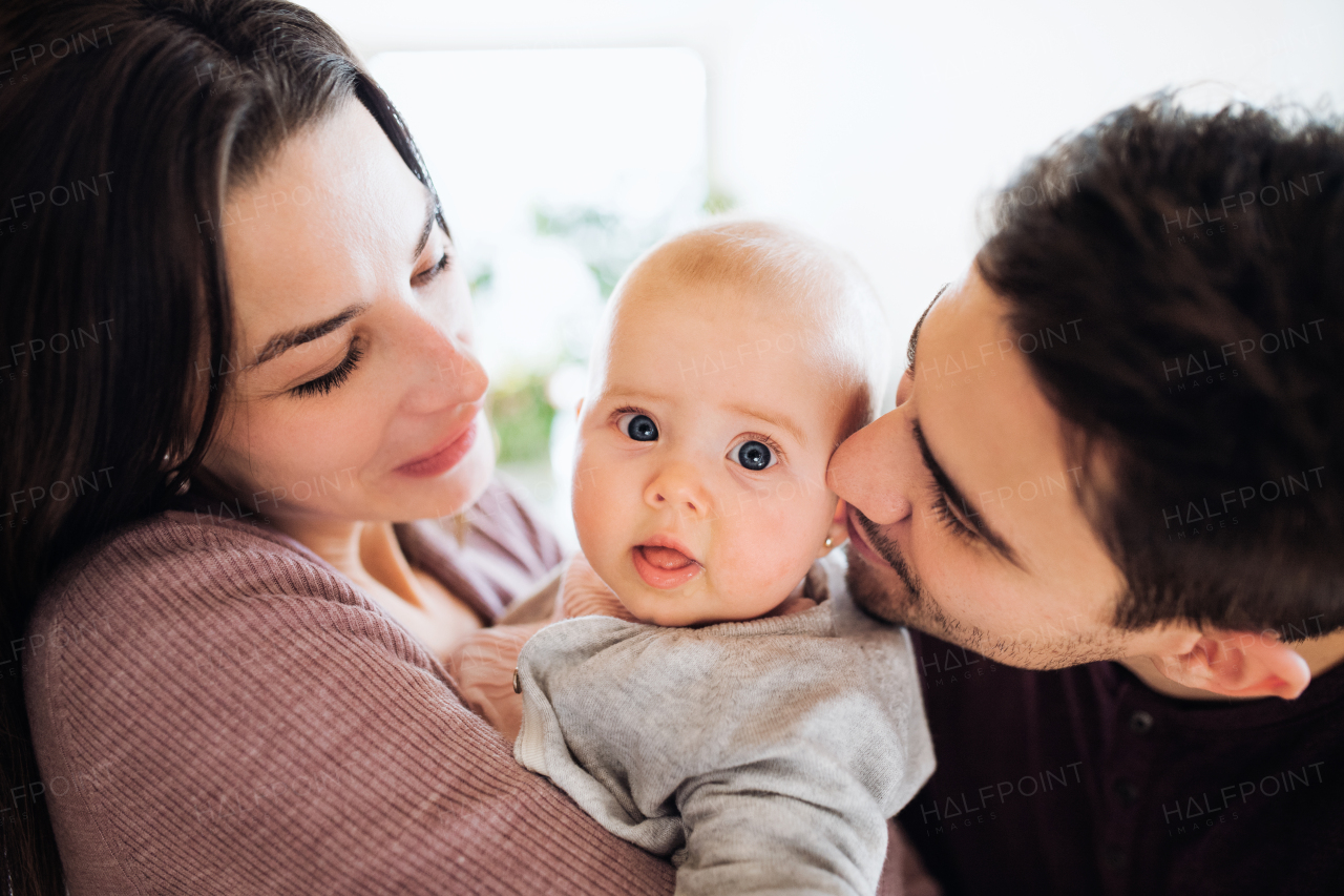 A close-up portrait of happy young couple with a baby indoors at home.