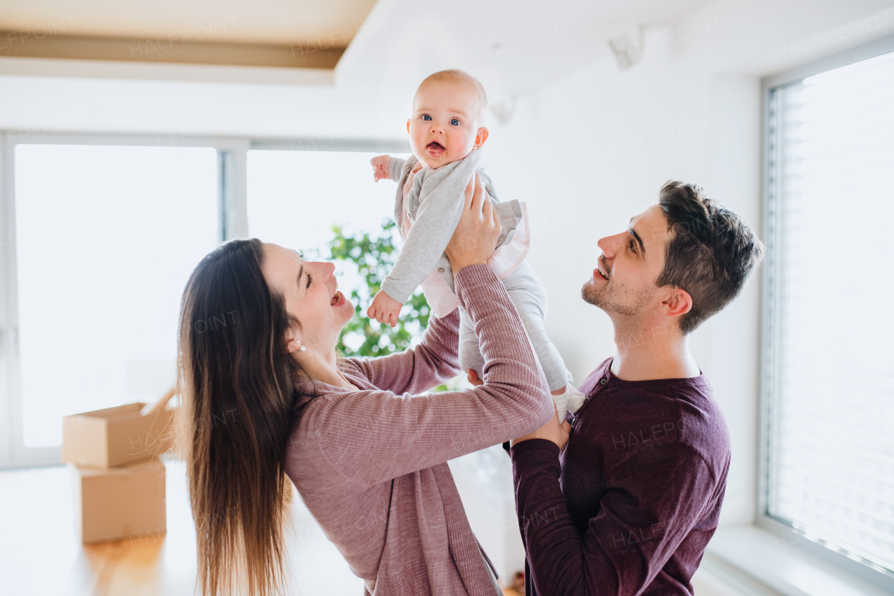 A portrait of happy young couple with a baby and cardboard boxes, moving in a new home.