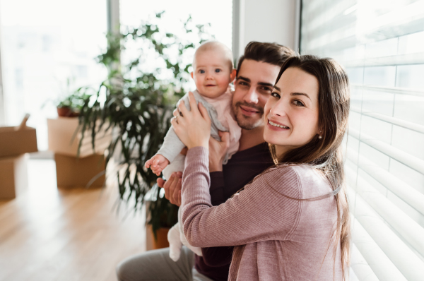 A portrait of happy young couple with a baby and cardboard boxes, moving in a new home.