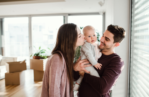 A portrait of happy young couple with a baby and cardboard boxes, moving in a new home.