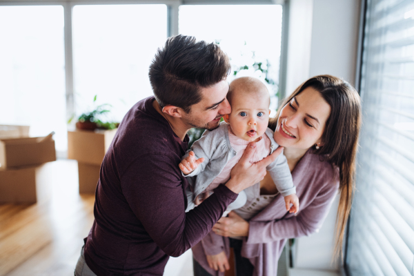 A portrait of happy young couple with a baby and cardboard boxes, moving in a new home.