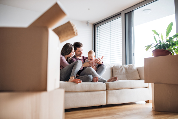 A portrait of happy young couple with a baby and cardboard boxes, moving in a new home.