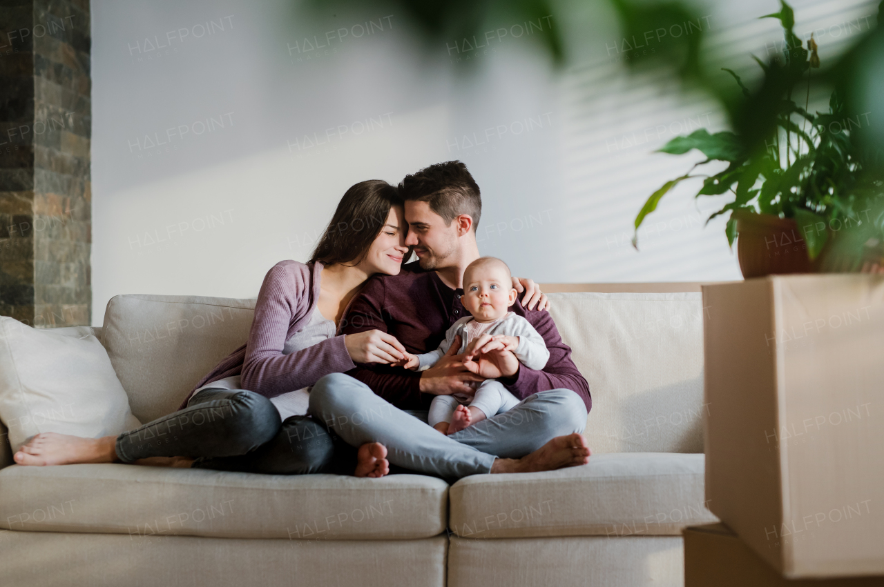 A portrait of happy young couple with a baby and cardboard boxes, moving in a new home.