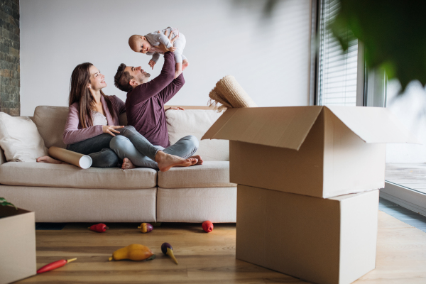 A portrait of happy young couple with a baby and cardboard boxes, moving in a new home.