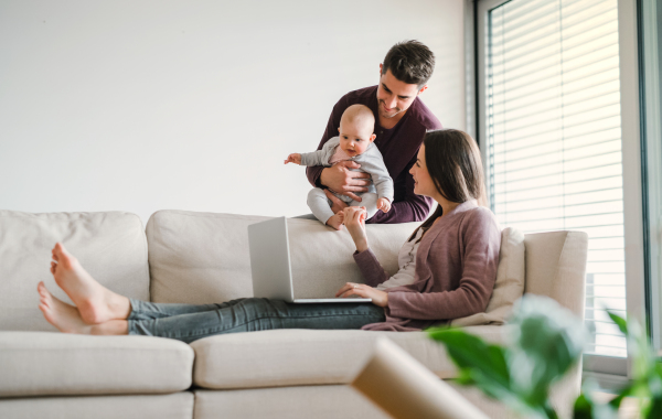 A portrait of young couple with a baby at home, using laptop. Copy space.