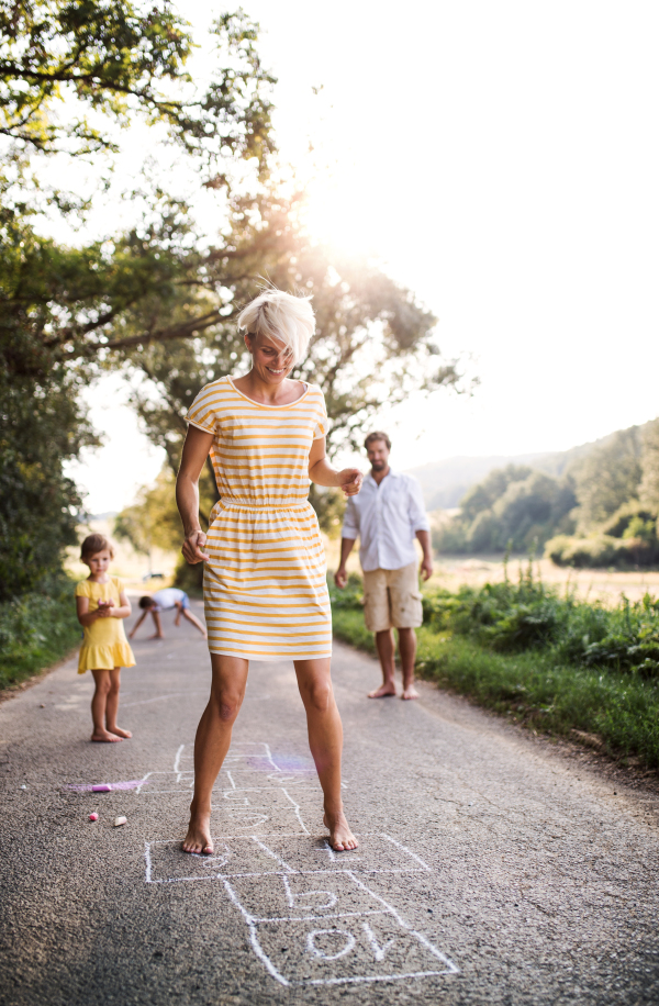 A young family with small children playing hopscotch on a road in countryside in summer.