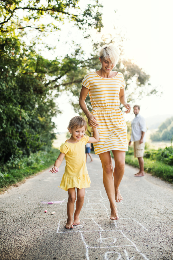 A young mother with small daughter playing hopscotch on a road in countryside in summer.