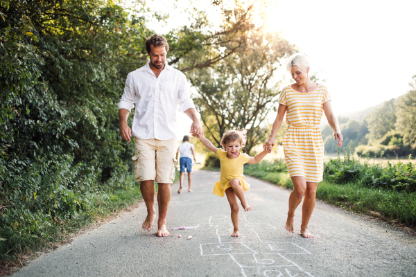 A young family with small children playing hopscotch on a road in countryside in summer.