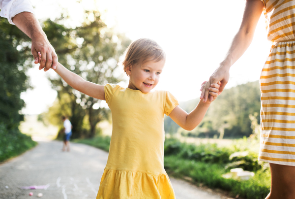 A midsection of family with small daughter playing hopscotch on a road in summer, holding hands.