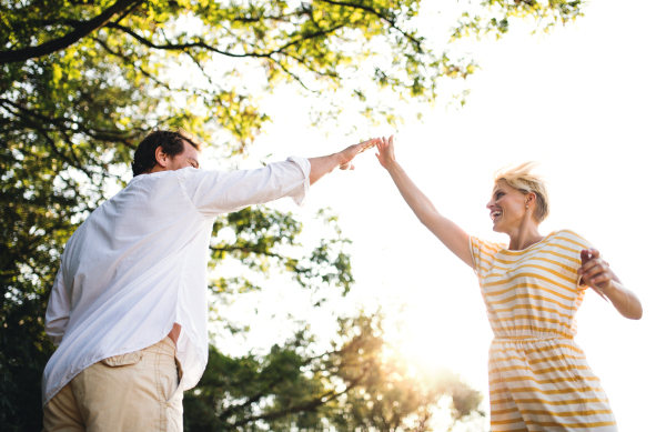 A cheerful young couple spending time together in nature in summer, making high five.