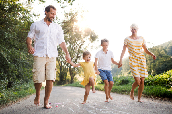 A young family with small children playing hopscotch on a road in countryside in summer.