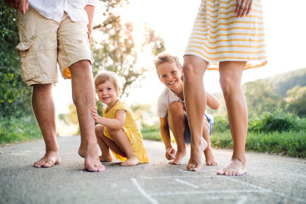 A midsection of young family with small children standing barefoot on a road in summer in countryside.