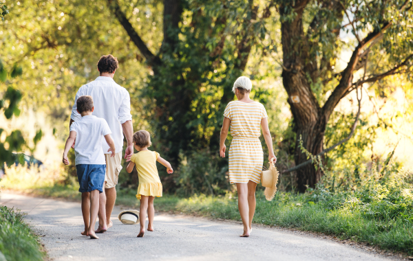 A rear view of young family with small children walking barefoot on a road in summer nature.