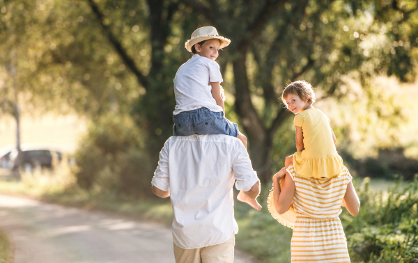 A rear view of happy young family with small children spending time together outside in green summer nature.