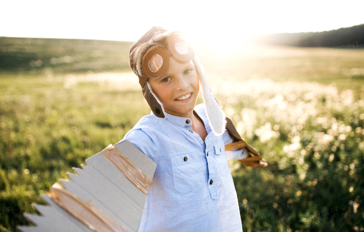 A small boy playing on a meadow in nature, with pilot goggles and wings as if flying.