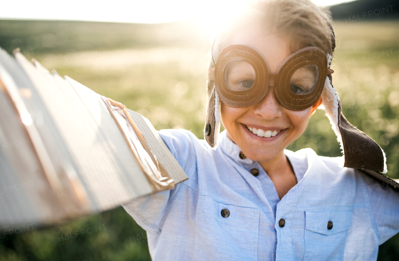 A small boy playing on a meadow in nature, with pilot goggles and wings as if flying.