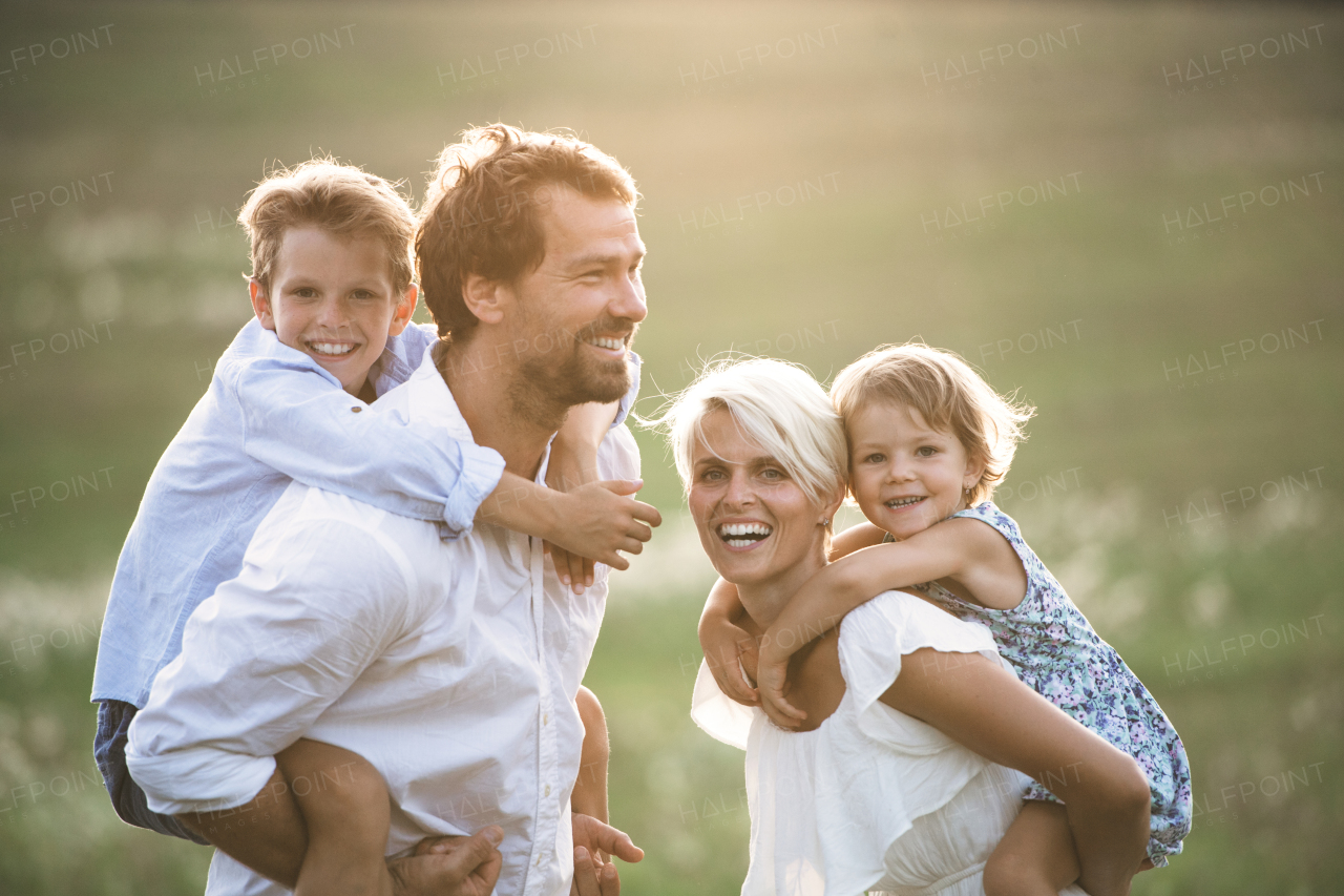 Happy young family with small children spending time together outside in green summer nature at sunset.