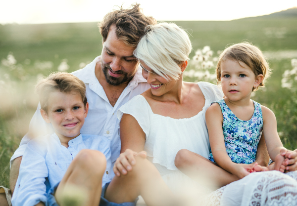 Happy young family with small children spending time together outside in green summer nature at sunset, sitting in the grass.