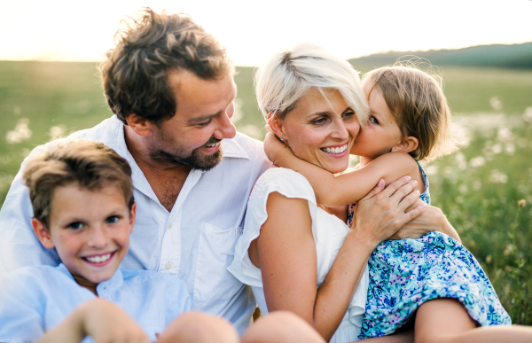 Happy young family with small children spending time together outside in green summer nature at sunset.