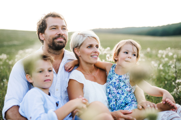 Happy young family with small children spending time together outside in green summer nature at sunset, sitting in the grass.