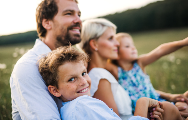 Happy young family with small children spending time together outside in green summer nature at sunset.