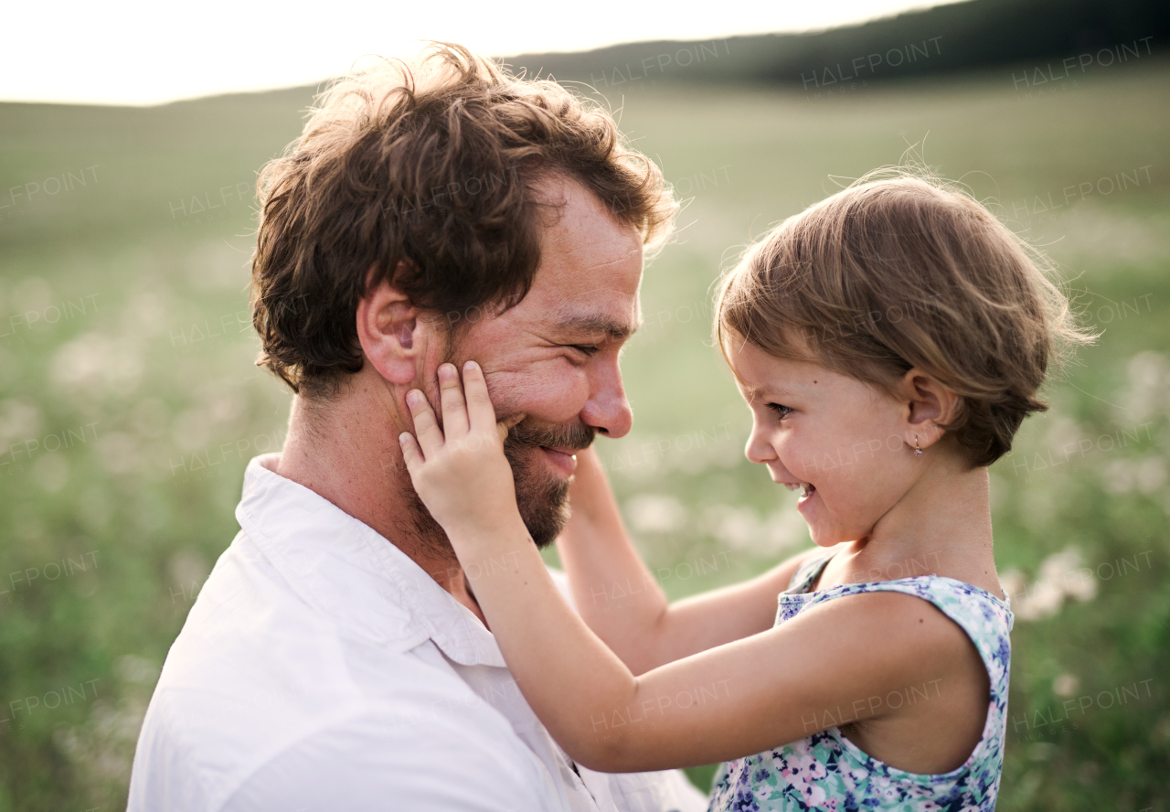 Handsome young father in green sunny summer nature holding his cute small daughter in the arms.