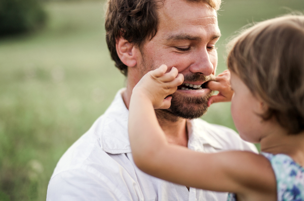 Handsome young father in green sunny summer nature holding his cute small daughter in the arms.