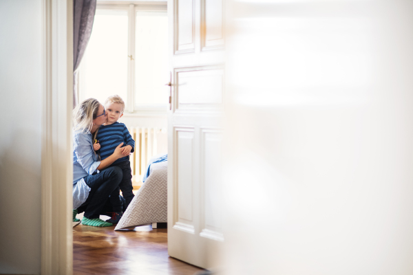 A young mother kissing her toddler son inside in a bedroom. Copy space.