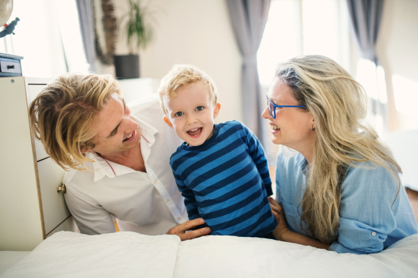 Happy young happy parents looking at their toddler son inside in a bedroom.