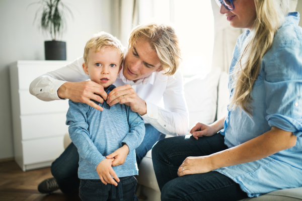 Young happy parents dressing on their toddler son inside in a bedroom.