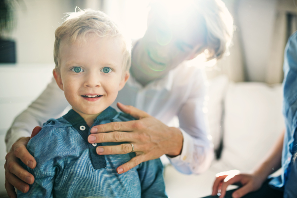 A happy toddler boy with young parents inside in a bedroom, dressing.