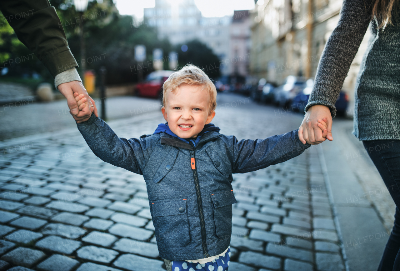 A small toddler boy with unrecognizable parents walking outdoors in city, holding hands.