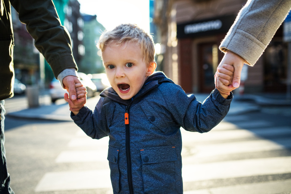 A small toddler boy with unrecognizable parents walking outdoors in city, holding hands.