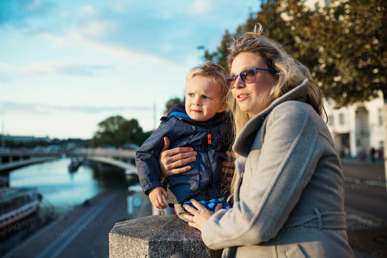 Young mother with her toddler son standing outdoors by the river in city of Prague.