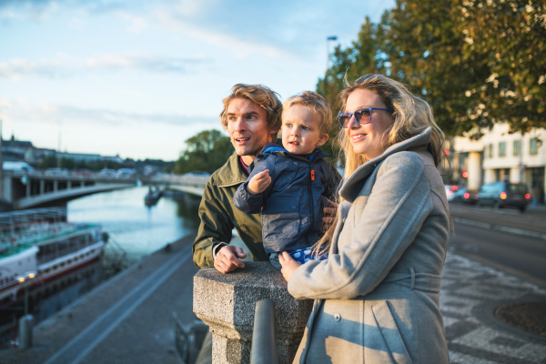 Young parents with their toddler son standing outdoors by the river in city of Prague.