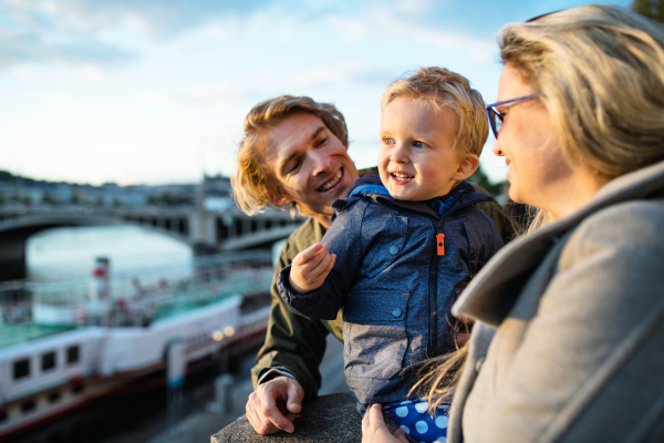 Young parents with their toddler son standing outdoors by the river in city of Prague.