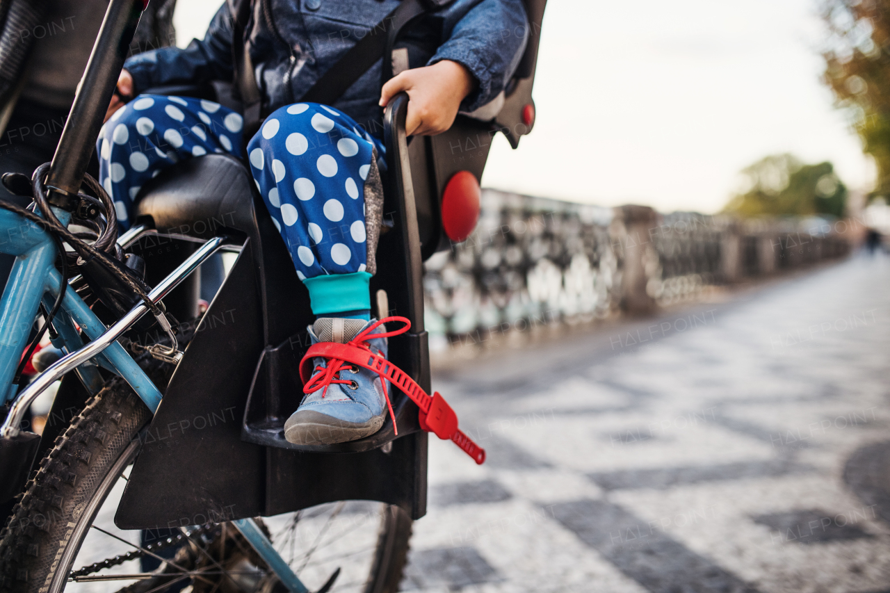 An unrecognizable small toddler boy sitting in bicycle seat with father outdoors on a street in city. Copy space.