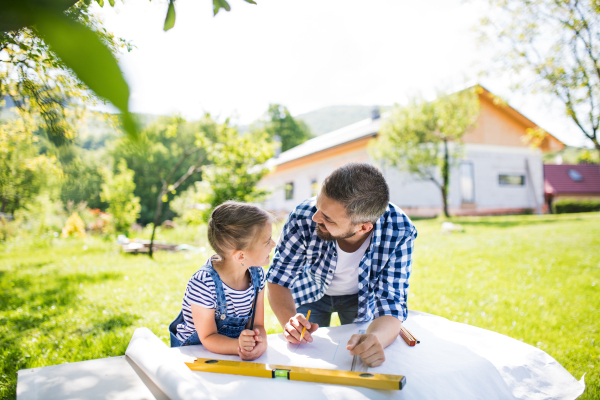 Mature father and a small daughter outside, planning wooden birdhouse or bird feeder. Sketches making.