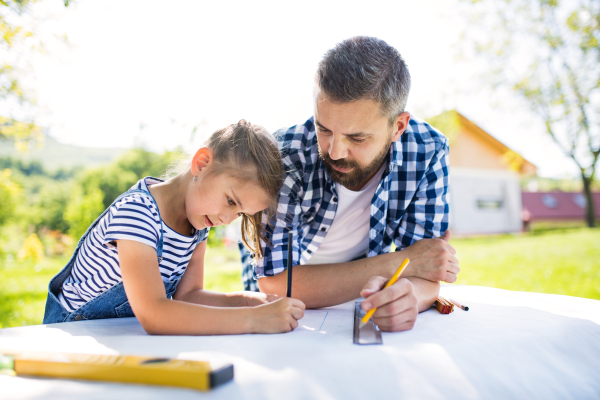 Mature father and a small daughter outside, planning wooden birdhouse or bird feeder. Sketches making.