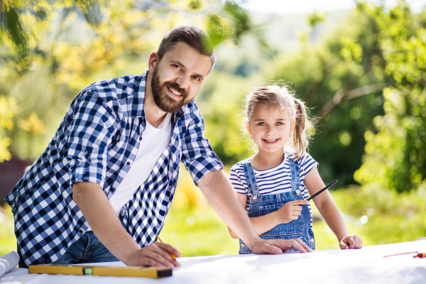 Father with a small daughter outside, planning wooden birdhouse or bird feeder. Sketches making.