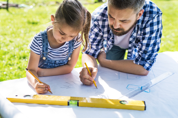 Mature father and a small daughter outside, planning wooden birdhouse or bird feeder. Sketches making.