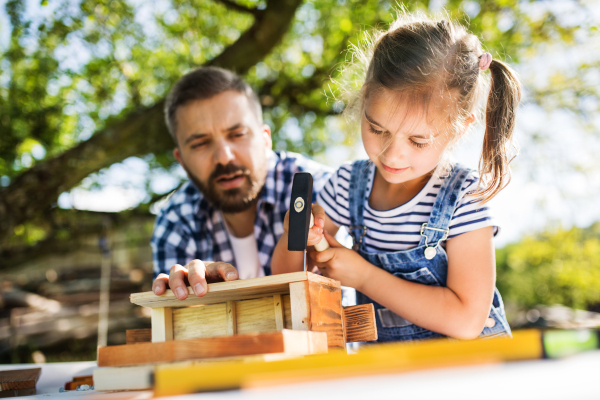 Father with a small daughter outside, making wooden birdhouse or bird feeder.