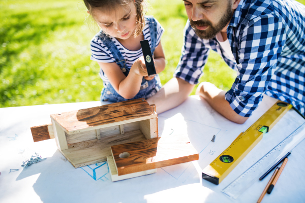 Father with a small daughter outside, making wooden birdhouse or bird feeder.