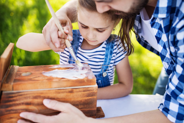 Unrecognizable father with a small daughter outside, making wooden birdhouse or bird feeder.